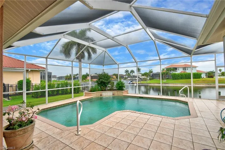 Screened pool enclosure featuring an irregular-shaped pool with integrated waterfall feature, waterside location, and tiled pool deck