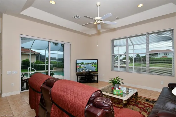 Living area featuring recessed tray ceiling, tile flooring, and multiple windows with horizontal blinds