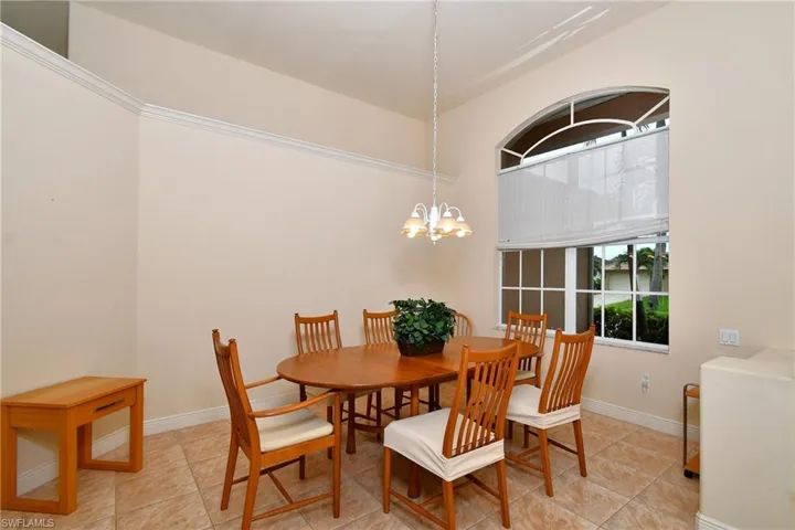 Dining area featuring a large arched window with decorative grilles, neutral wall tones, crown molding, a built-in light fixture, and tiled flooring