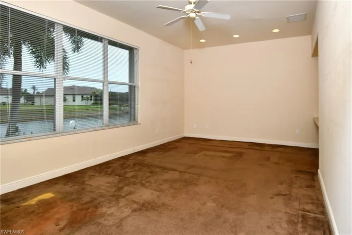 Spacious room featuring broad windows with horizontal blinds overlooking a canal, a ceiling fan, recessed lighting, and a built-in shelf