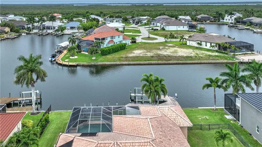 Waterfront property featuring a private boat dock, screened pool enclosure, mature palm trees, and manicured green spaces