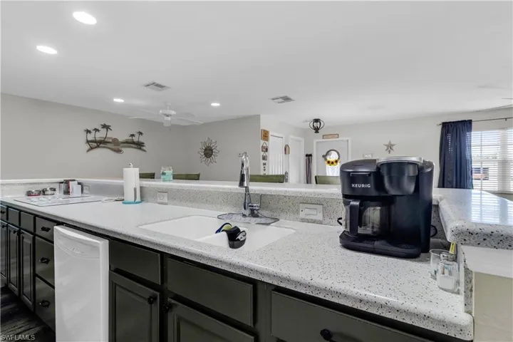 Kitchen featuring white speckled countertops, an undermount sink with a gooseneck faucet, dark cabinetry, and recessed lighting