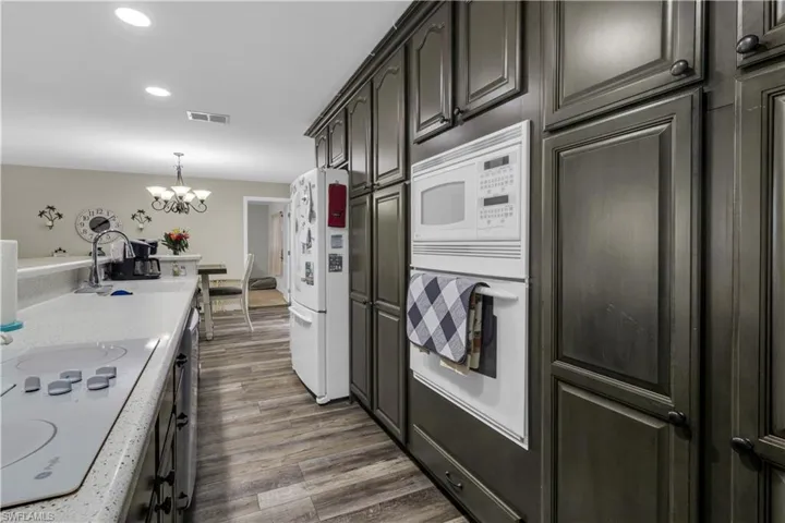 Galley kitchen featuring extensive dark wood cabinetry, white built-in appliances, light-toned countertops, and wood-finish flooring