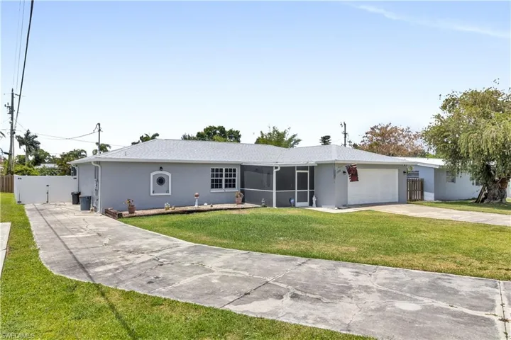 Single-story residence featuring a light gray exterior, a screened entry, an attached garage, a paved driveway, and a front lawn