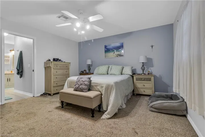 Carpeted bedroom featuring a ceiling fan with integrated lighting, a contrasting accent wall, and a doorway opening to a bathroom with a double vanity