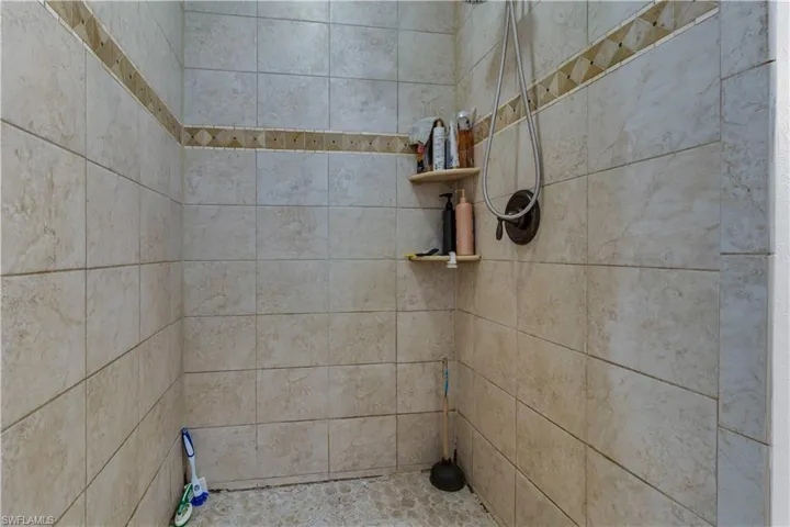 Walk-in shower with neutral-toned rectangular wall tiles, decorative accent tile band, and pebble-finish floor