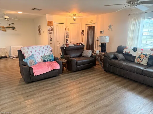 Spacious interior featuring wood-finish flooring, a ceiling fan with light fixture, and a window with blinds and sheer curtains