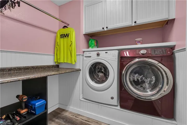 Dedicated laundry area featuring a built-in counter, upper cabinetry with black hardware, white beadboard paneling, and a chrome hanging rod