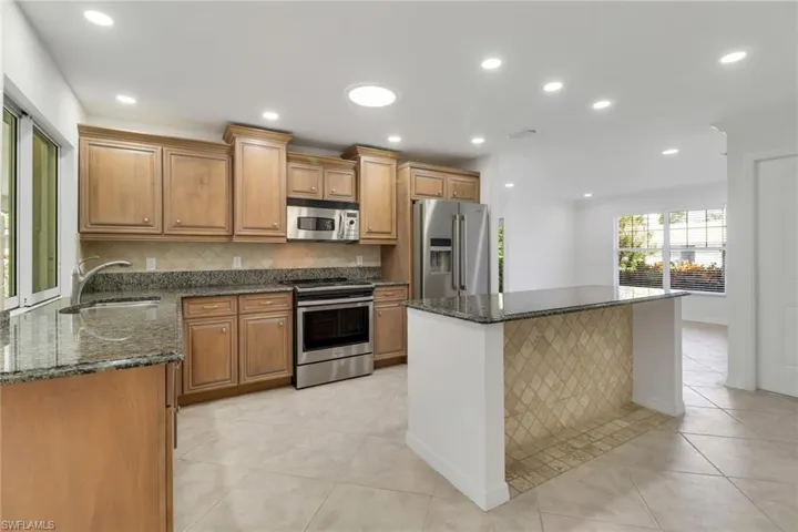 Kitchen featuring dark stone counters, appliances with stainless steel finishes, decorative backsplash, a kitchen island, and recessed lighting