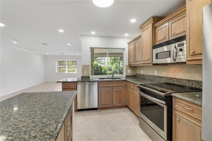 Kitchen featuring stainless steel appliances, light tile patterned floors, decorative backsplash, dark stone countertops, and recessed lighting