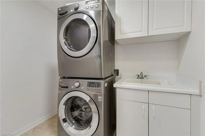 Laundry area featuring cabinet space, stacked washing machine and dryer, and light tile patterned floors