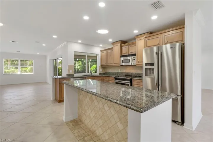 Kitchen featuring stainless steel appliances, decorative backsplash, dark stone counters, light tile patterned floors, and recessed lighting