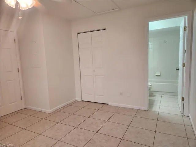 Unfurnished bedroom featuring light tile patterned flooring, electric panel, a closet, and connected bathroom