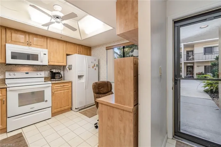 Kitchen featuring white appliances, neutral tile floors, and ceiling fan