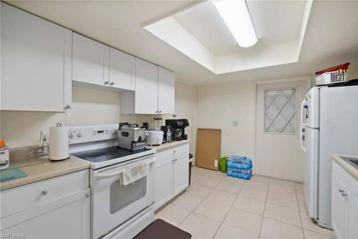 Kitchen featuring white cabinetry, light tile patterned floors, white appliances, and a raised ceiling