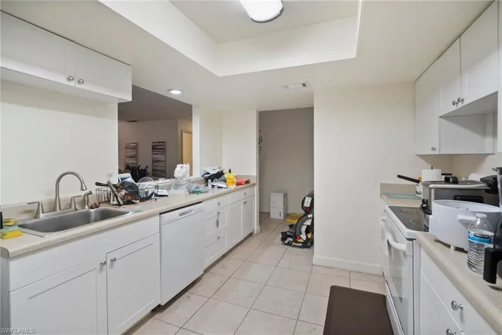 Kitchen with white cabinetry, sink, light tile patterned floors, a tray ceiling, and white appliances