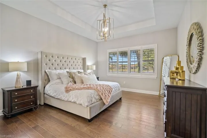 Bedroom with a notable chandelier, a raised ceiling, and dark wood-type flooring