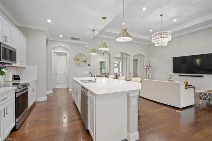 Kitchen featuring light stone counters, stainless steel appliances, a kitchen island with sink, white cabinetry, and hanging light fixtures