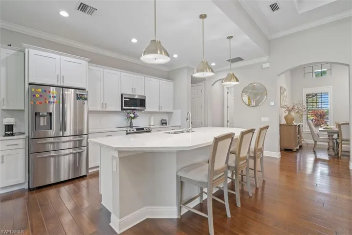 Kitchen with white cabinetry, sink, hanging light fixtures, a center island with sink, and appliances with stainless steel finishes