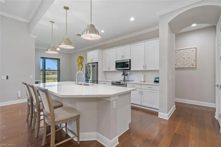 Kitchen featuring a center island with sink, decorative light fixtures, white cabinetry, and appliances with stainless steel finishes