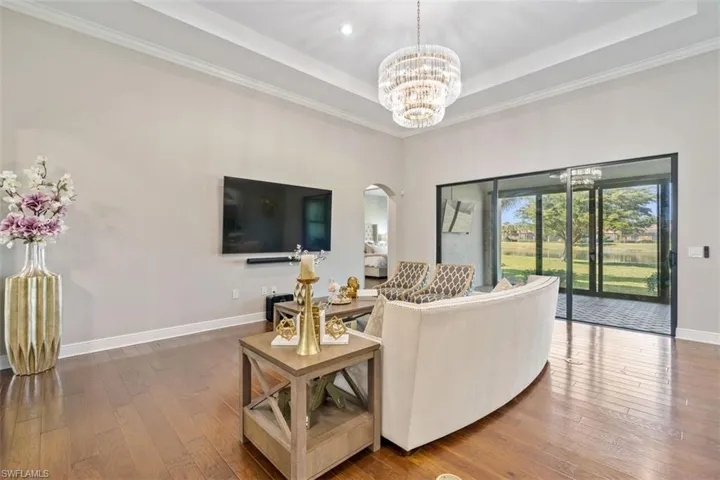 Living room featuring a notable chandelier, a raised ceiling, wood-type flooring, and crown molding