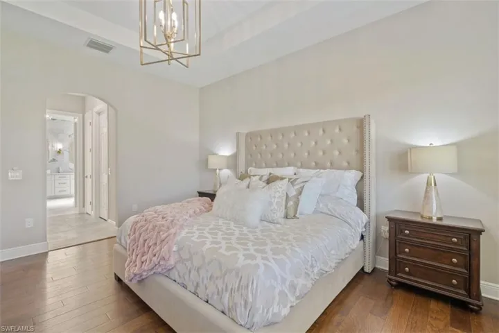 Bedroom with dark hardwood / wood-style flooring, connected bathroom, and an inviting chandelier