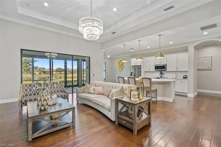 Living room featuring dark wood-type flooring, a raised ceiling, a notable chandelier, and crown molding
