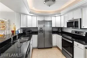 Kitchen with appliances with stainless steel finishes, a tray ceiling, white cabinets, and light tile patterned flooring