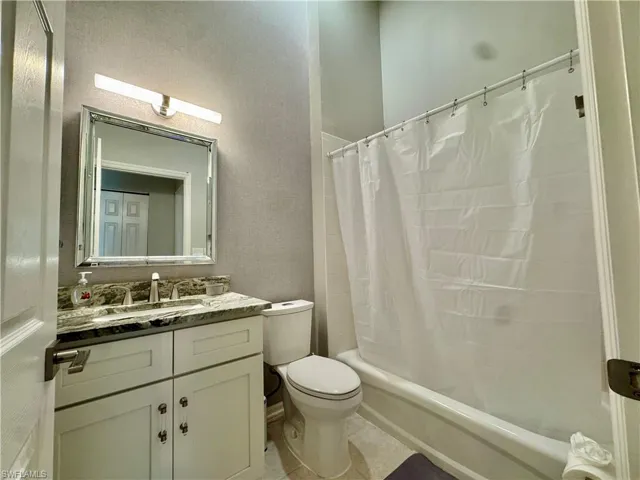 Bathroom with shower / tub combo, vanity, light tile patterned floors, and a textured wall