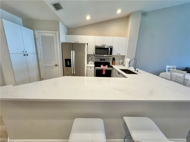 Kitchen featuring a kitchen bar, a peninsula, appliances with stainless steel finishes, lofted ceiling, and white cabinetry