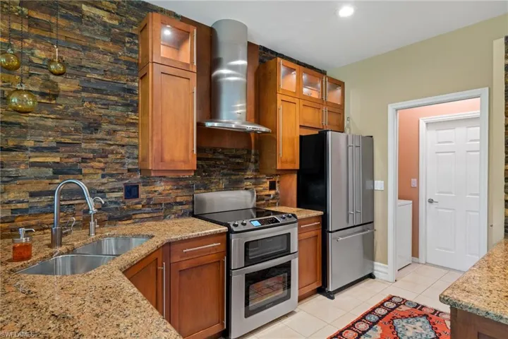 Kitchen featuring appliances with stainless steel finishes, wall chimney range hood, sink, light tile patterned floors, and light stone countertops