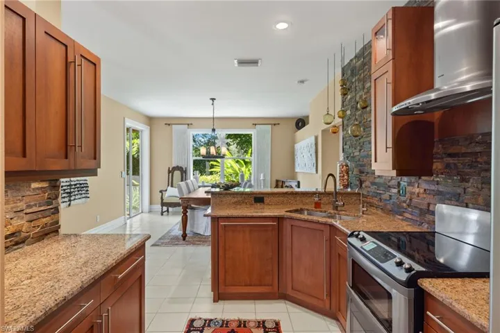 Kitchen featuring sink, light tile patterned floors, decorative backsplash, electric range, and wall chimney exhaust hood