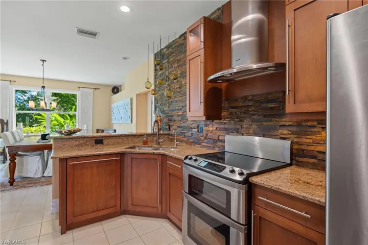 Kitchen with stainless steel appliances, wall chimney range hood, sink, hanging light fixtures, and light tile patterned floors