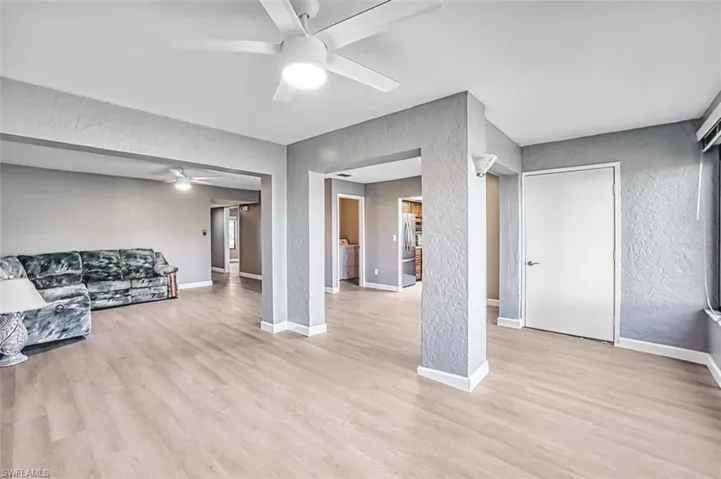 Unfurnished living room with a ceiling fan, a textured wall, and light wood finished floors