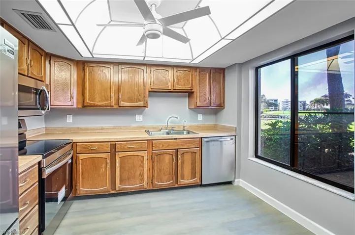 Kitchen featuring appliances with stainless steel finishes, light countertops, ceiling fan, light wood-style floors, and brown cabinets