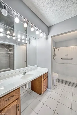 Bathroom with vanity, light tile patterned floors, a textured ceiling, and a spacious closet