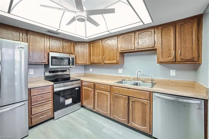 Kitchen with appliances with stainless steel finishes, light countertops, brown cabinets, and a ceiling fan