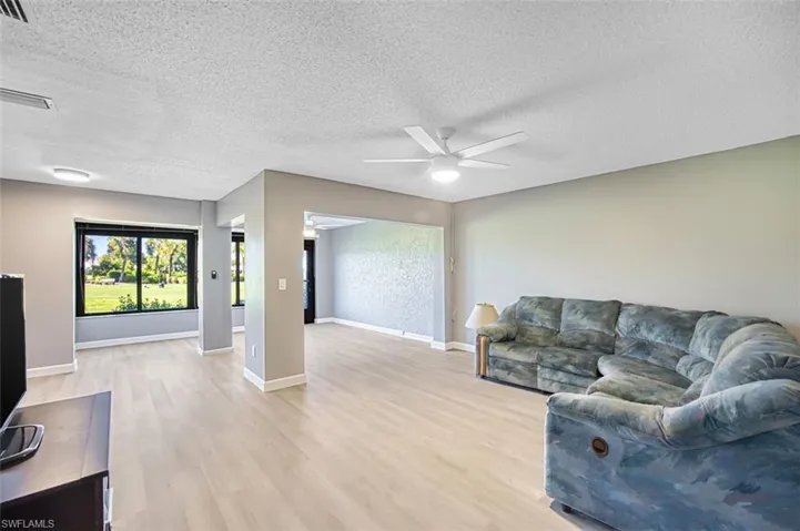 Living area featuring a textured ceiling, light wood-type flooring, and a ceiling fan