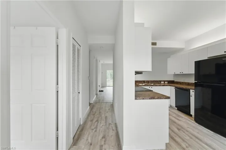 Kitchen featuring black appliances, dark countertops, light wood-type flooring, and white cabinets