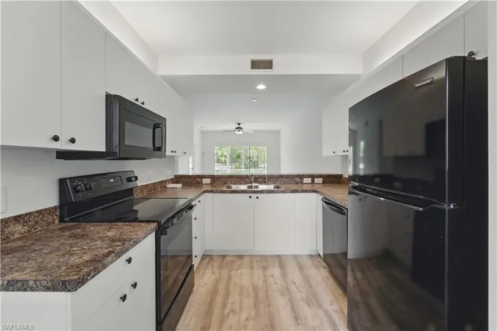 Kitchen with black appliances, dark countertops, light wood-type flooring, white cabinets, and recessed lighting