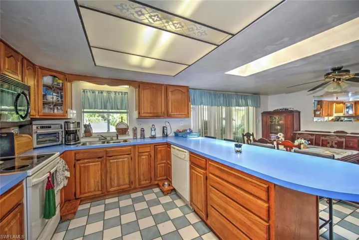 Kitchen with a breakfast bar area, white appliances, kitchen peninsula, light tile patterned flooring, and ceiling fan