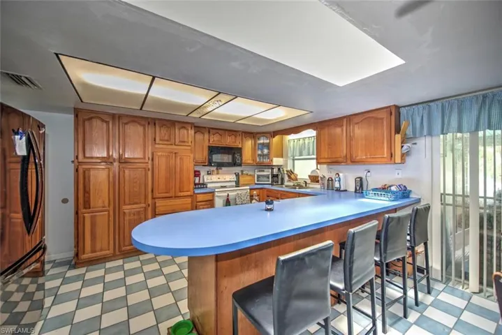 Kitchen with light tile patterned floors, kitchen peninsula, white range with electric stovetop, fridge, and a kitchen bar