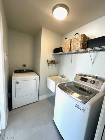 Clothes washing area with washing machine and clothes dryer, baseboards, laundry area, a sink, and light tile patterned floors