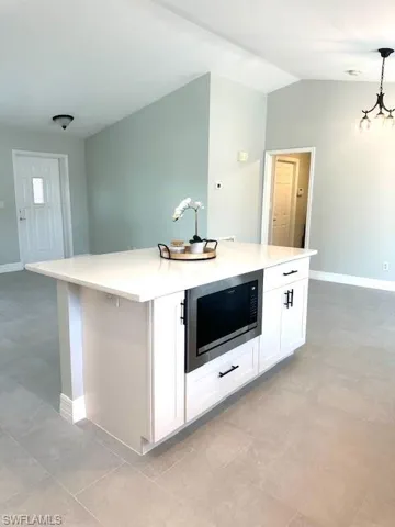 Kitchen with a kitchen island, hanging light fixtures, lofted ceiling, stainless steel microwave, and white cabinets