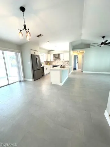 Kitchen with backsplash, freestanding refrigerator, open floor plan, wall chimney range hood, and visible vents