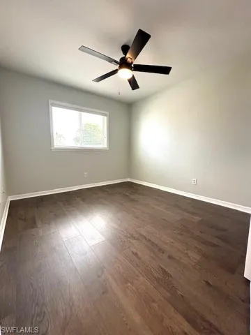 Spare room featuring dark wood finished floors, baseboards, and ceiling fan