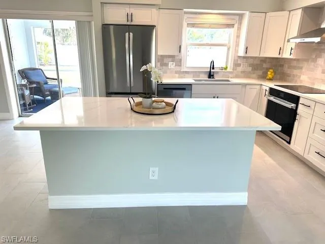 Kitchen featuring a wealth of natural light, wall chimney exhaust hood, a sink, and stainless steel appliances