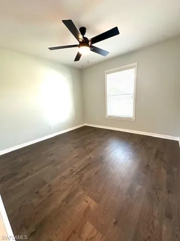 Unfurnished room with baseboards, dark wood-style floors, and a ceiling fan