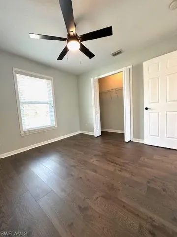 Unfurnished bedroom featuring a closet, a ceiling fan, baseboards, visible vents, and dark wood-type flooring