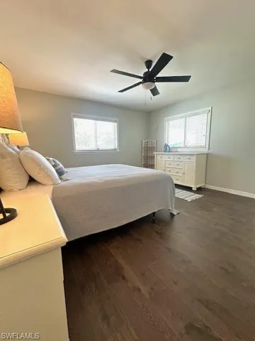 Bedroom with dark wood-style floors, multiple windows, ceiling fan, and baseboards